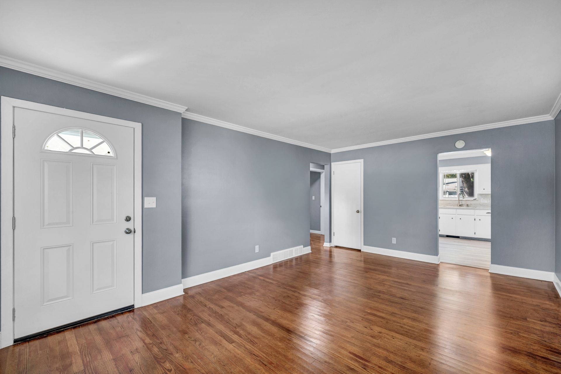 An empty living room with grey walls, hardwood floors, and a white front door